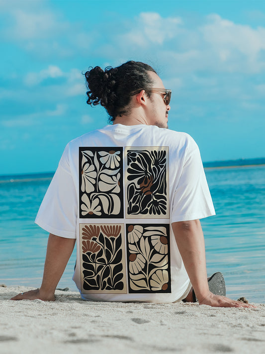 Person sitting on a beach wearing a white t-shirt with a geometric pattern on the back.